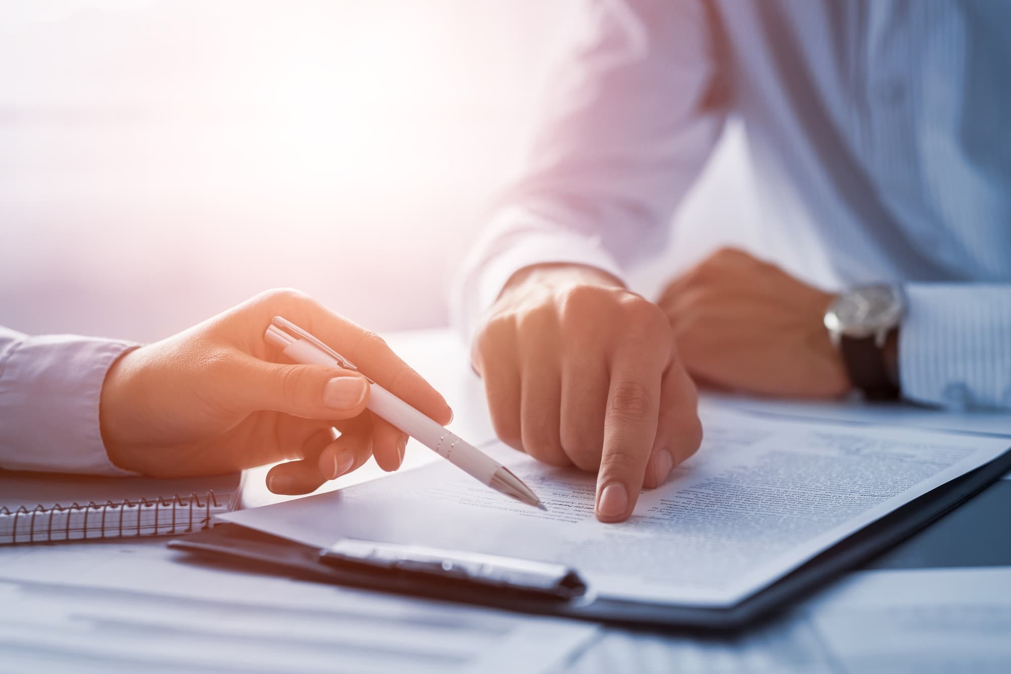 Close-up of two people reviewing a document, with one pointing and the other holding a pen.